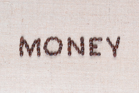 Money word from roasted coffee beans on creamy linen canvas, shot from above, close up.