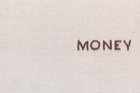 Money word from roasted coffee beans on creamy linen canvas, shot from above, aligned middle right.の写真素材