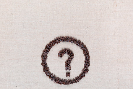 Question mark enclosed in circle made from coffee beans on creamy linen fabric, shot from above, aligned bottom center.の写真素材