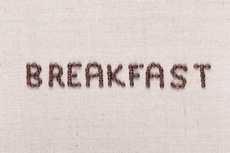 Breakfast word written with coffee beans on creamy linea canvas, shot from above, aligned in center,close up.の写真素材