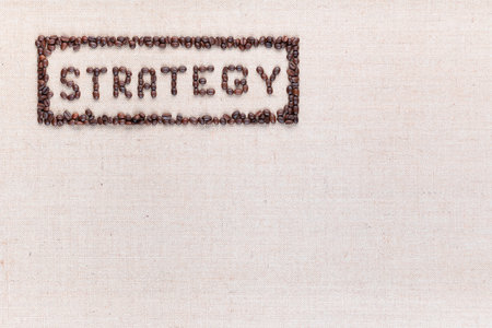 The word Strategy inside a rectangle written with coffee beans on creamy linea canvas, shot from above, aligned at the top left.の写真素材