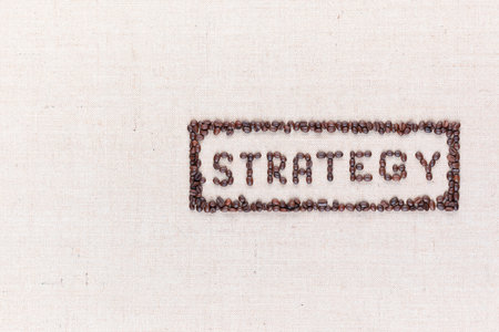The word Strategy inside a rectangle written with coffee beans on creamy linea canvas, shot from above, aligned to the right.の写真素材