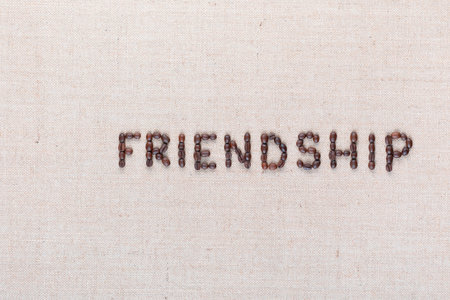 Friendship word written with coffee beans on creamy linea canvas, shot from above, aligned to the right.の写真素材