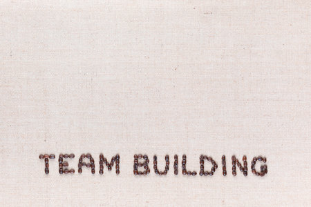 The words Team Building written with coffee beans on creamy linea canvas, shot from above, aligned at the bottom.の写真素材