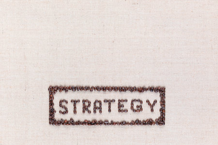 The word Strategy inside a rectangle written with coffee beans on creamy linea canvas, shot from above,aligned at the bottom.の写真素材
