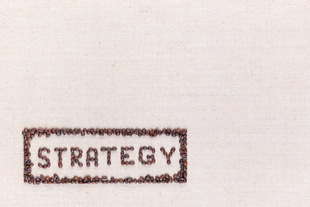 The word Strategy inside a rectangle written with coffee beans on creamy linea canvas, shot from above, aligned at the bottom left.の写真素材