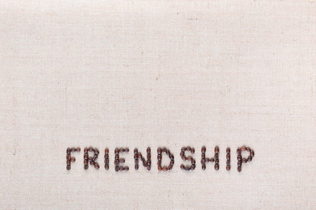 Friendship word written with coffee beans on creamy linea canvas, shot from above, aligned at the bottom.の写真素材