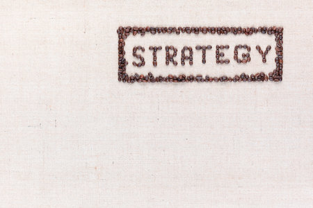 The word Strategy inside a rectangle written with coffee beans on creamy linea canvas, shot from above, aligned to the top right.の写真素材