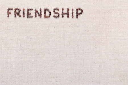 Friendship word written with coffee beans on creamy linea canvas, shot from above, aligned at the top left.の写真素材