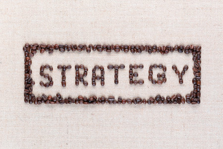 The word Strategy inside a rectangle written with coffee beans on creamy linea canvas, shot from above,aligned in the center,close up.の写真素材