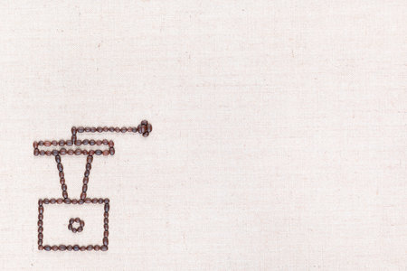 A coffee grinder made from coffee beans on creamy linea canvas, shot from above , aligned at the bottom left.の写真素材