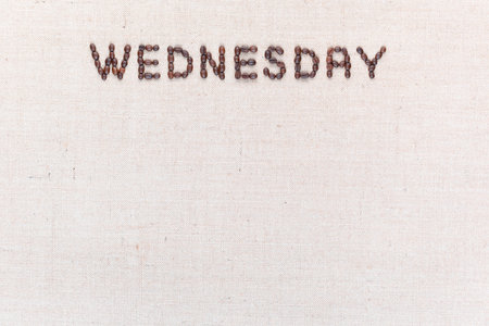 The word Wednesday written with coffee beans on creamy linea canvas, shot from above , aligned at the top.の写真素材