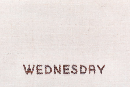 The word Wednesday written with coffee beans on creamy linea canvas, shot from above , aligned at the bottom.の写真素材