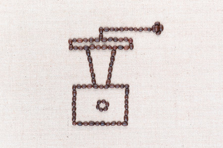 A coffee grinder made from coffee beans on creamy linea canvas, shot from above , aligned in the center, closeup.の写真素材