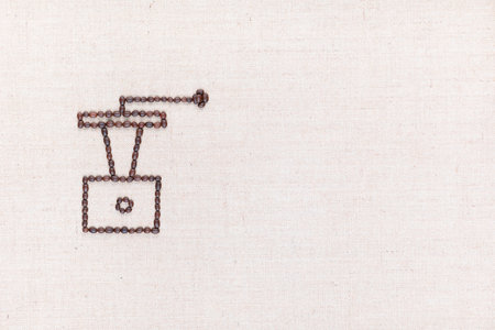 A coffee grinder made from coffee beans on creamy linea canvas, shot from above , aligned to the left.の写真素材