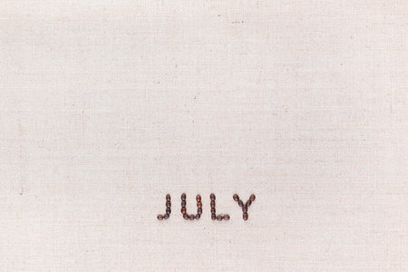 The word July written with coffee beans on creamy linea canvas, shot from above, aligned at the bottom.の写真素材