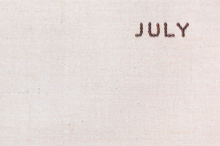The word July written with coffee beans on creamy linea canvas, shot from above, aligned at the top right.の写真素材