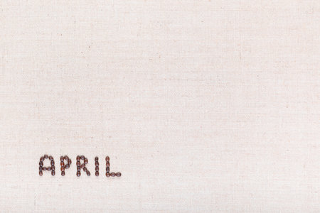 The word April written with coffee beans on creamy linea canvas, shot from above, aligned at the bottom left.の写真素材