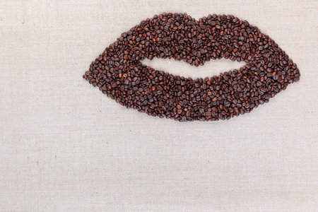 Open female lips made with coffee beans on creamy linea canvas, shot from above, aligned at the top right.の写真素材