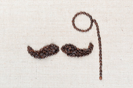 A monocle and a mustache all made with coffee beans on creamy linea canvas, shot from above, aligned in the center, closeup.の写真素材