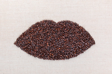 Closed female lips made with coffee beans on creamy linea canvas, shot from above, aligned in the center.の写真素材