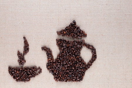 Roasted coffee beans forming steamy cup and pot on linen surface, aligned at the bottom leftの写真素材