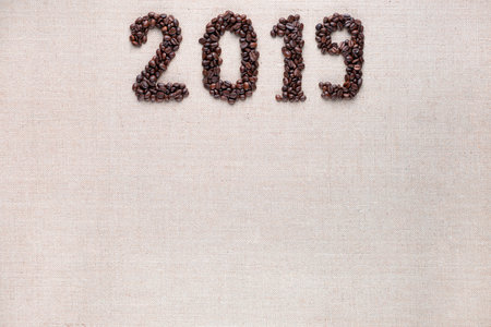Bunch of fresh roasted coffee beans forming 2019 inscription on creamy linen canvas, aligned top centerの写真素材