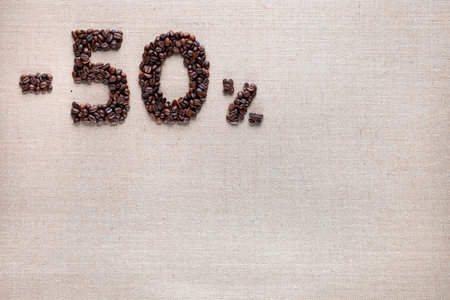 Roasted coffee beans shaping 50% off writing on creamy linen background, aligned top leftの写真素材
