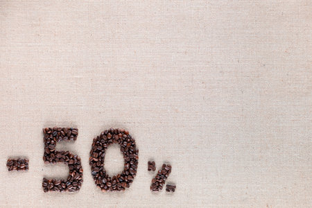 Roasted coffee beans shaping 50% off writing on creamy linen background, aligned bottom leftの写真素材