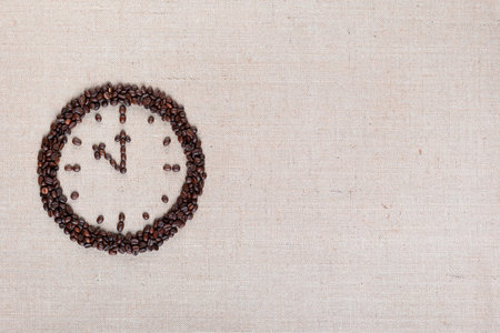 Round clock made of roasted beans representing coffee time on linen surface, arranged to the leftの写真素材