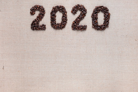 Bunch of fresh roasted coffee beans forming 2020 inscription on creamy linen canvas, aligned top centerの写真素材