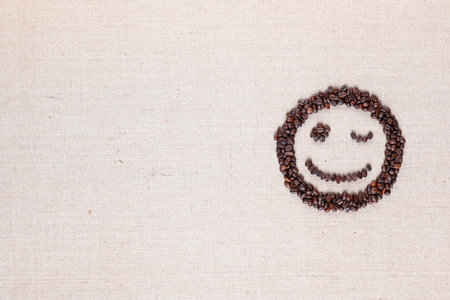 Adorable blinking smiling face made of roasted coffee beans against creamy linen background, aligned middle rightの写真素材