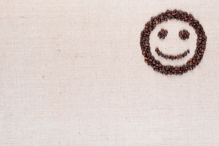 Adorable smiling face made of roasted coffee beans against creamy linen background, aligned top...