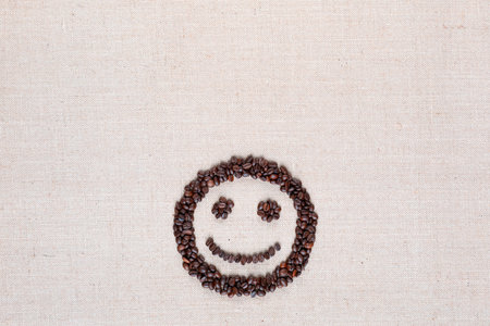 Adorable smiling face made of roasted coffee beans against creamy linen background, aligned bottom centerの写真素材