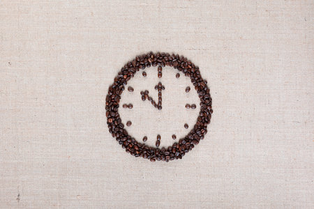 Round clock made of roasted beans representing coffee time on linen surface, arranged in centerの写真素材