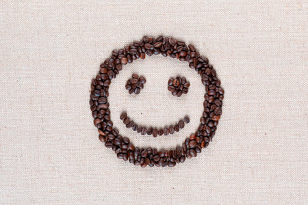 Adorable smiling face made of roasted coffee beans against creamy linen background, shot close upの写真素材