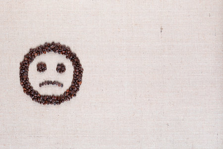 Sad round smile icon made of coffee beans on creamy linen texture, arranged middle leftの写真素材