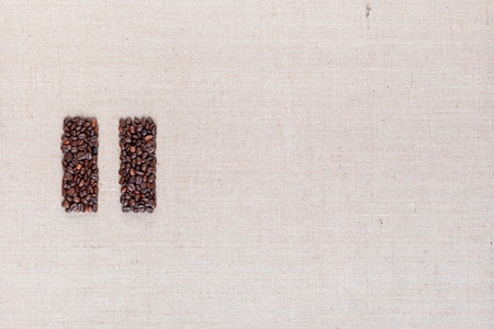 Bunch of roasted coffee beans forming pause symbol on creamy linen canvas, arranged middle leftの写真素材