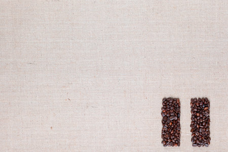 Bunch of roasted coffee beans forming pause symbol on creamy linen canvas, arranged bottom rightの写真素材