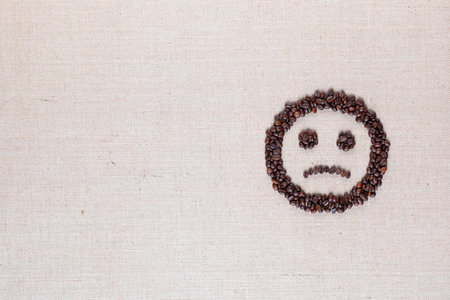 Sad round smile icon made of coffee beans on creamy linen texture, arranged middle rightの写真素材
