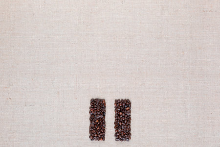 Bunch of roasted coffee beans forming pause symbol on creamy linen canvas, arranged bottom centerの写真素材