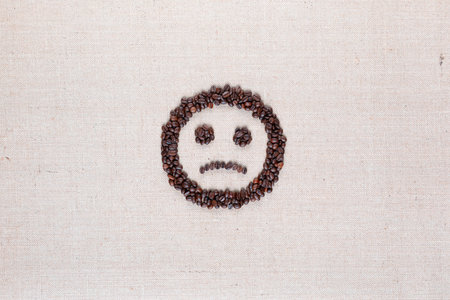 Sad round smile icon made of coffee beans on creamy linen texture, arranged in centerの写真素材