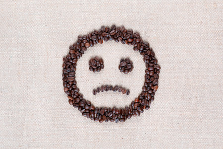 Sad round smile icon made of coffee beans on creamy linen texture, shot close upの写真素材