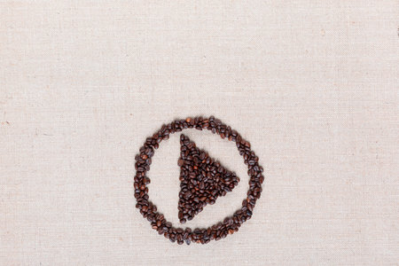 Bunch of roasted coffee beans forming play symbol enclosed in circle on creamy linen canvas, arranged bottom centerの写真素材