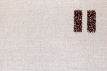 Bunch of roasted coffee beans forming pause symbol on creamy linen canvas, arranged top rightの写真素材
