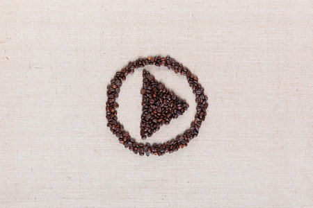 Bunch of roasted coffee beans forming play symbol enclosed in circle on creamy linen canvas, arranged in centerの写真素材