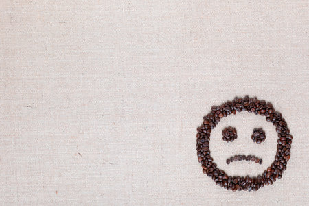 Sad round smile icon made of coffee beans on creamy linen texture, arranged bottom rightの写真素材