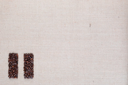 Bunch of roasted coffee beans forming pause symbol on creamy linen canvas, arranged bottom leftの写真素材