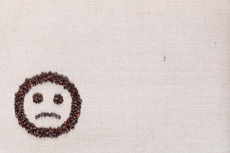 Sad round smile icon made of coffee beans on creamy linen texture, arranged bottom leftの写真素材