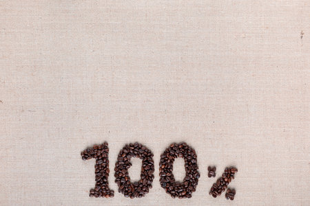 Roasted coffee beans shaping 100% off writing on creamy linen background, aligned bottom centerの写真素材
